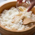Sushi rice being gently mixed with vinegar in a wooden bowl for a glossy restaurant-style finish