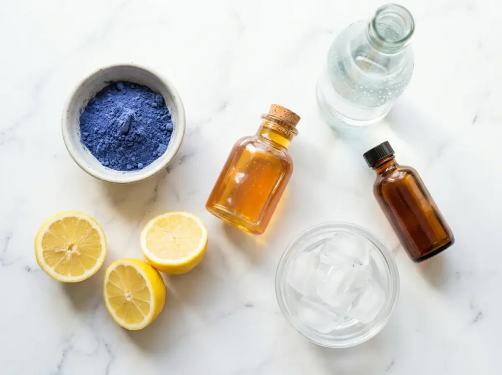 Lotus drink ingredients flatlay on white marble: butterfly pea flower powder, lemons, honey, sparkling water, vanilla